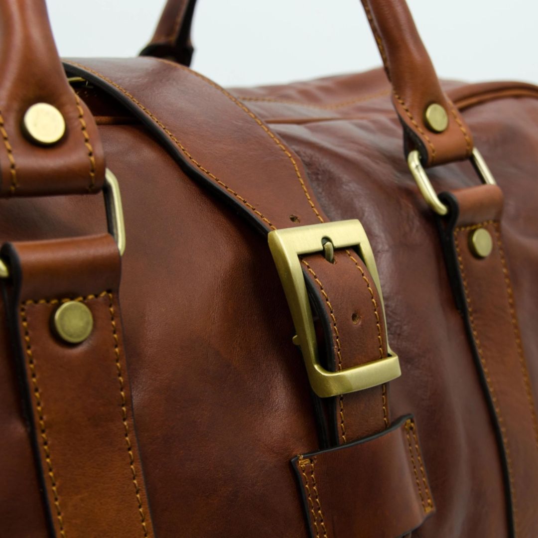 Close-up of a brown leather bag with gold buckles and studs.